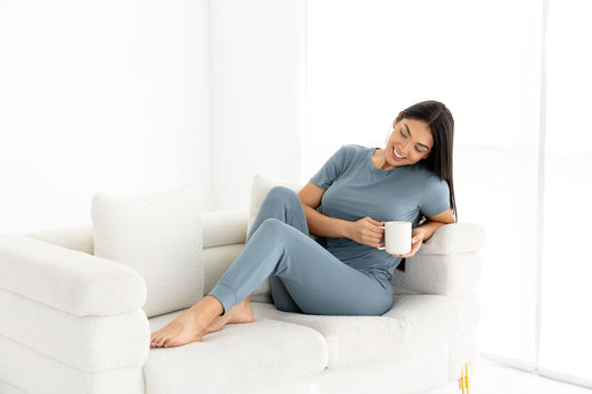 Woman lounging in women modal pajama set, French blue, crew neck top and joggers, relaxing on white sofa with a coffee mug.