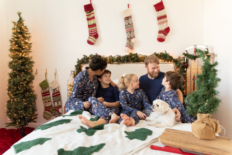 Family in matching Woodland Night pajamas on a bed with their dog