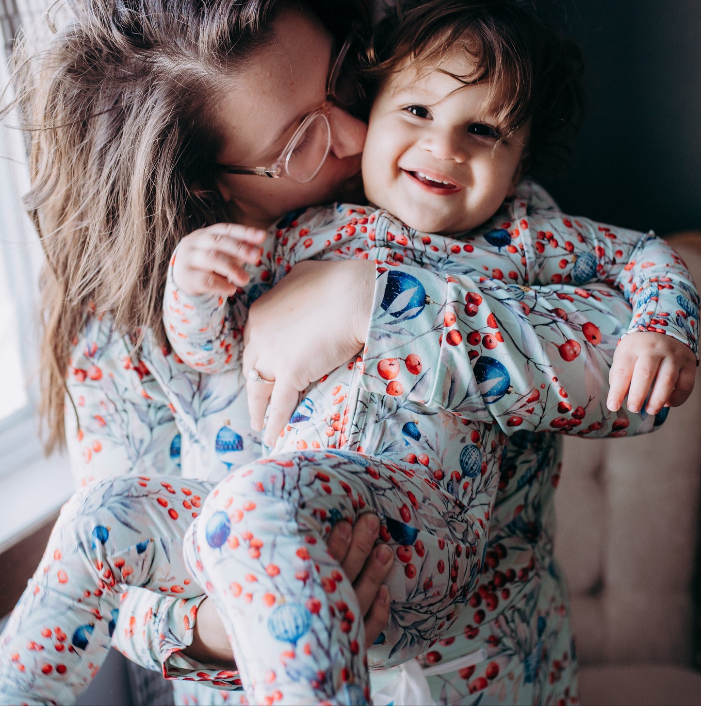 Two children in matching pajamas hugging in a room with a window.