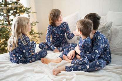 Four children in matching pajamas sitting on a bed with a Christmas tree in the background