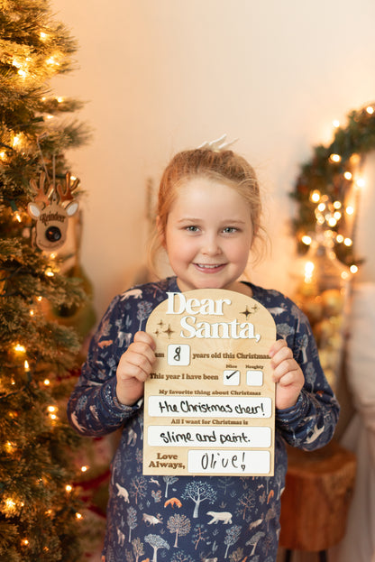 Child holding a personalized Christmas letter in front of a decorated Christmas tree.