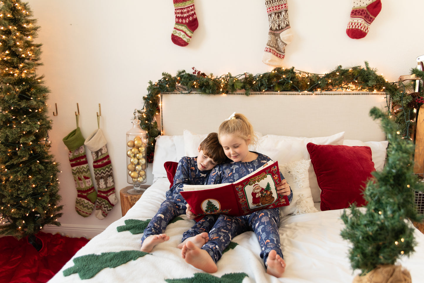 Two children reading a book on a bed decorated for Christmas.