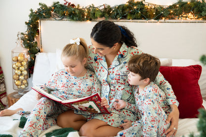 Woman and two children in matching pajamas reading a book on a couch with Christmas decorations.